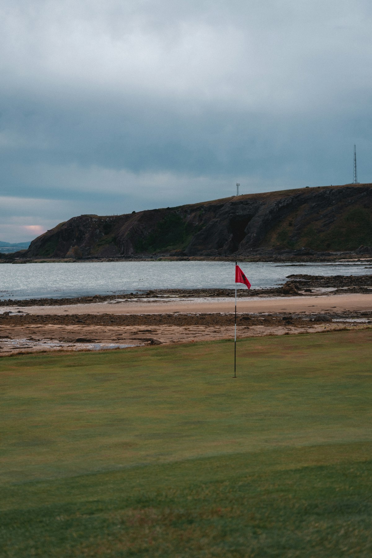 Placeholder image: a red pin flag on a green beside a cold grey sea and headland
