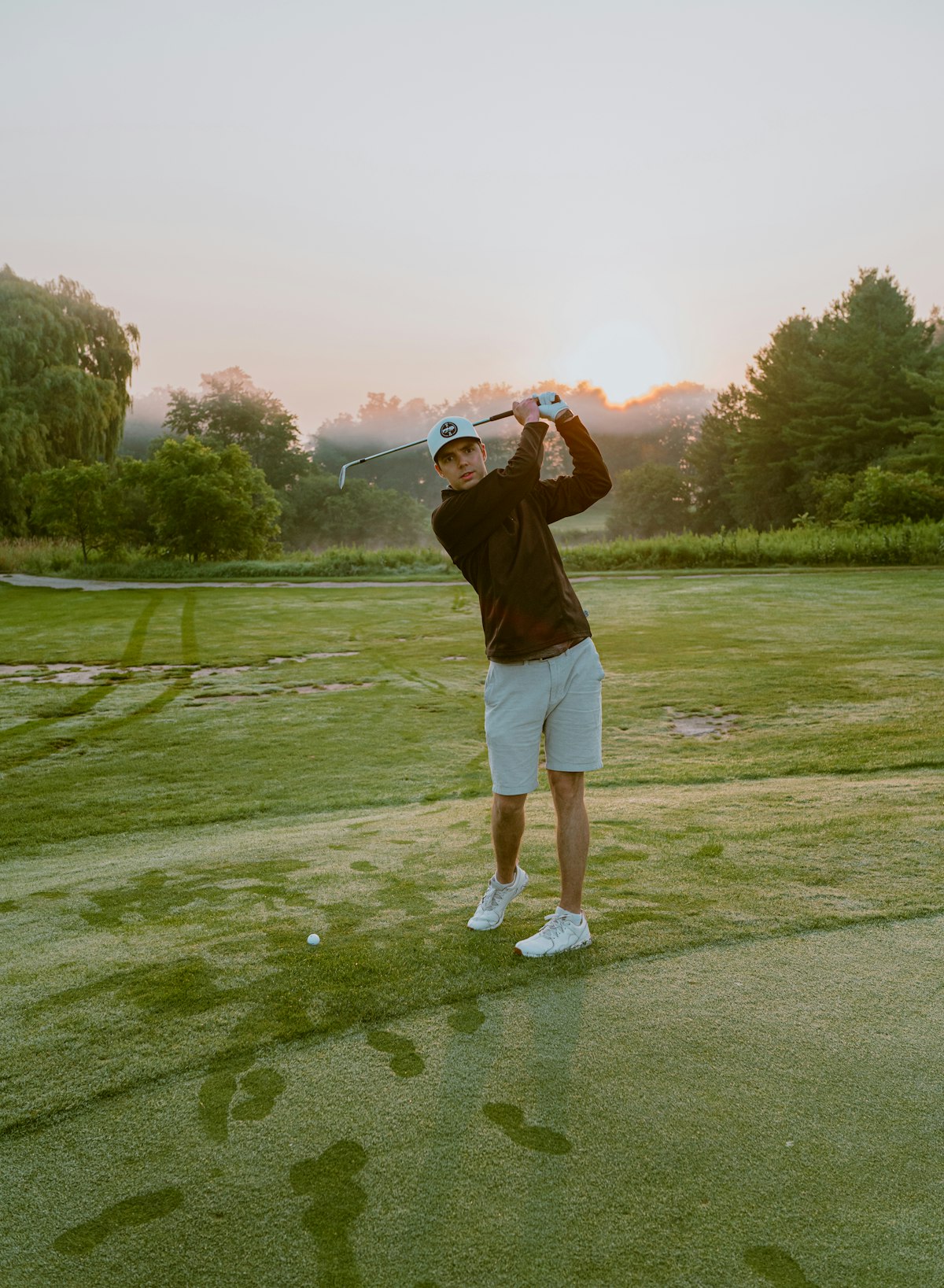 Placeholder image: a golfer mid-swing at misty sunrise on a tree-lined course